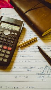 kalkulator leżący na zeszycie obok długopisu i notesu