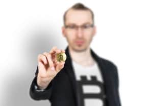 Biały mężczyzna trzymający w dłoni monetę Bitcoin