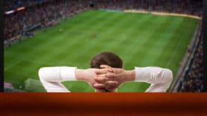 człowiek trzymający ręce za głową i oglądający mecz